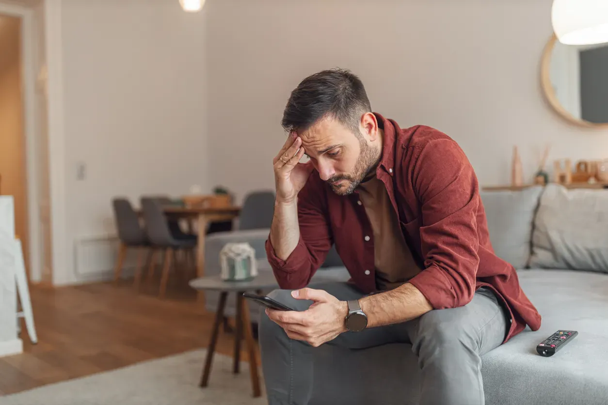 Mann sitzt auf Sofa und sucht in seinem Smartphone